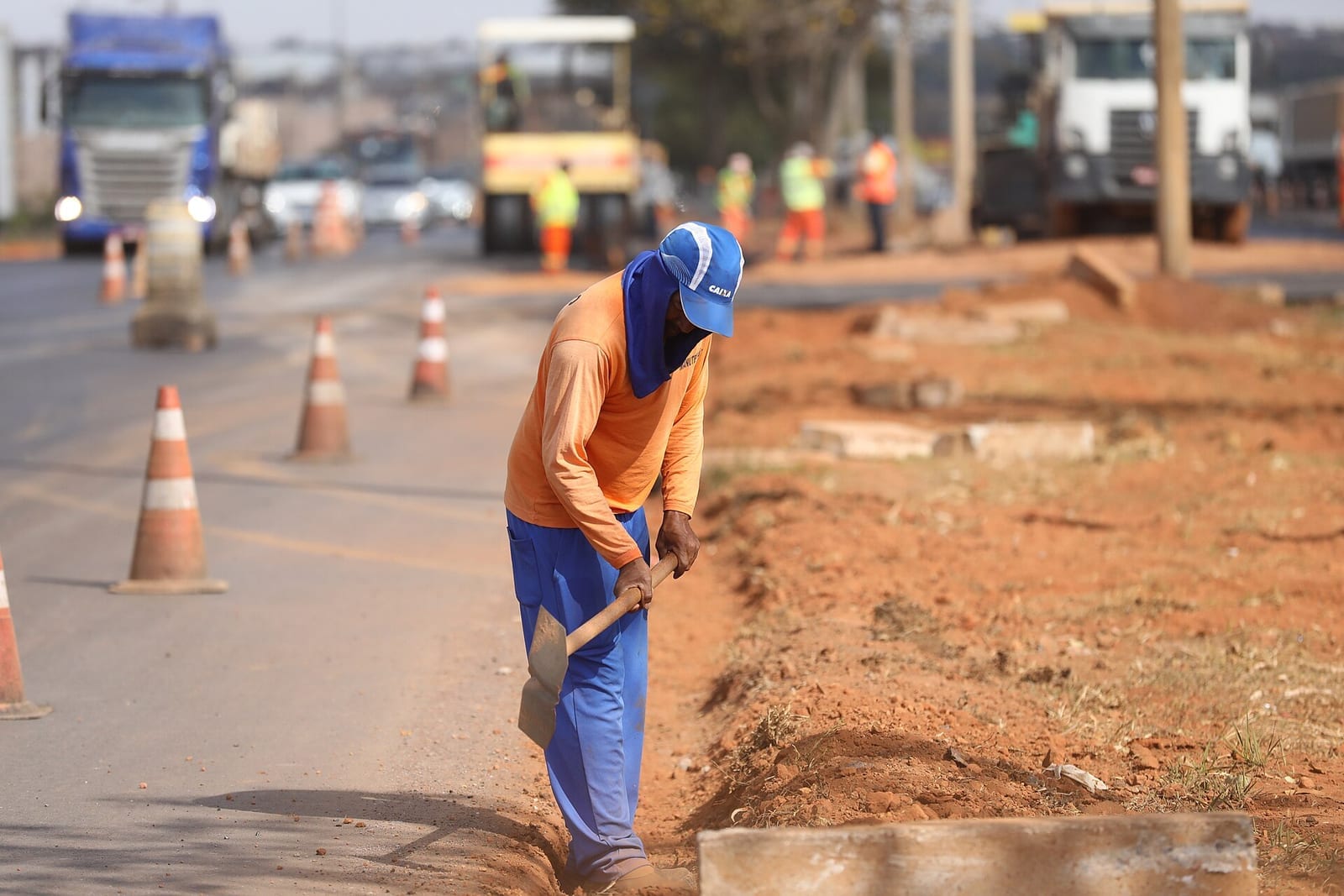 Trabalhador de uniforme laranja cavando à beira de uma rodovia em obras